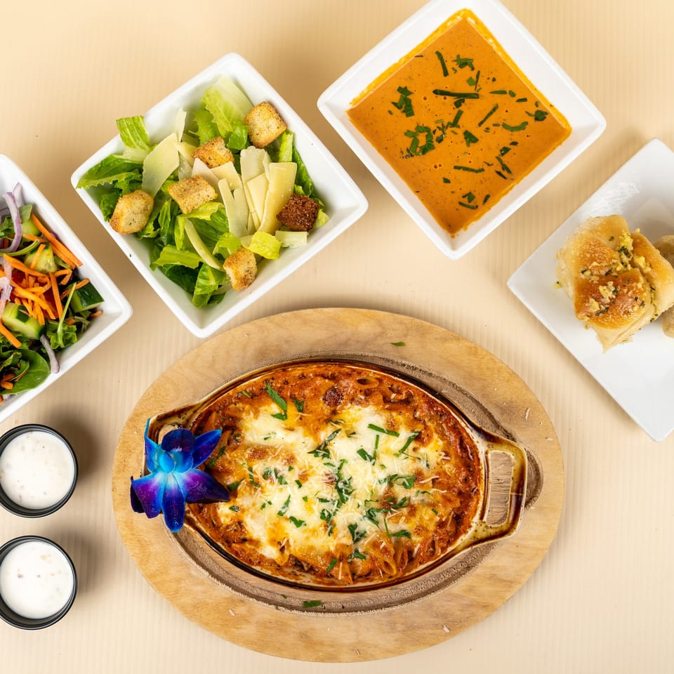 Baked ziti with melted cheese, Caesar salad, garden salad, tomato soup, and garlic knots.
