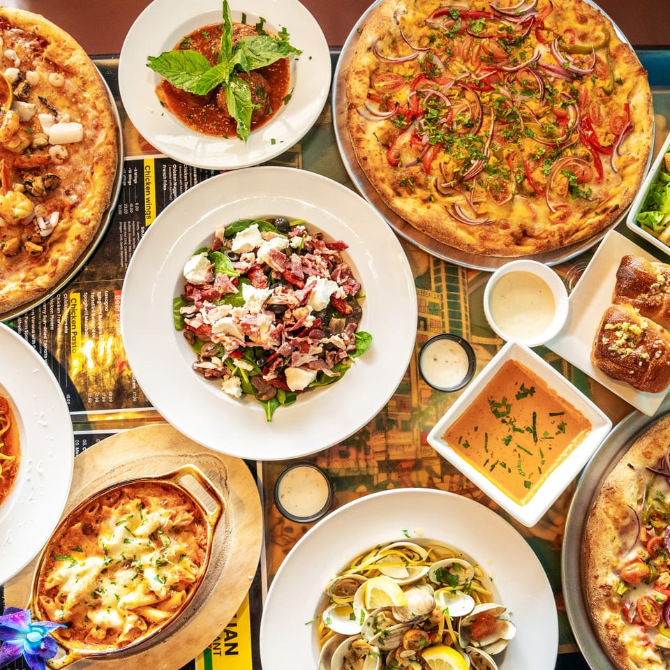 A vibrant spread of Italian dishes including pizzas, pasta, salad, meatballs, and garlic knots.