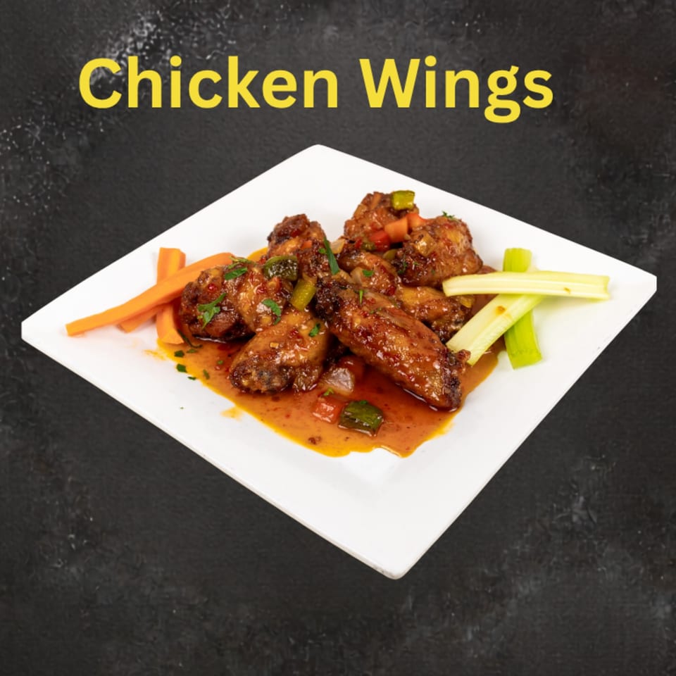Glazed chicken wings garnished with herbs and peppers, served with carrot and celery sticks on a white plate.