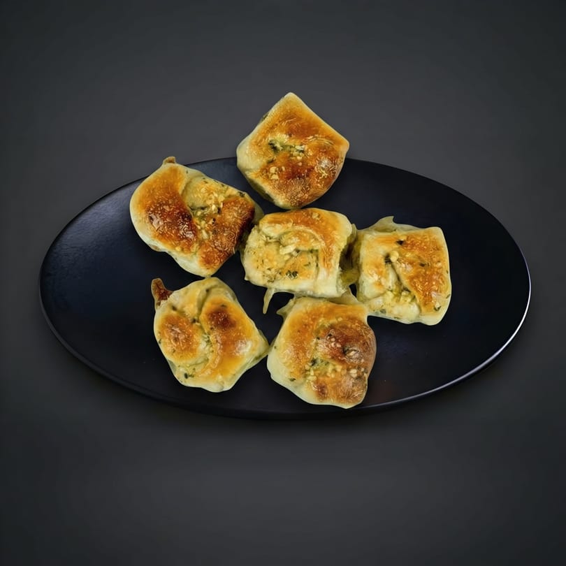 Six golden-brown savory pastries with green herbs and cheese on a black plate.