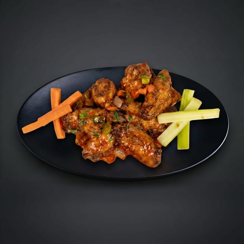 Sweet and sour chicken wings with chopped vegetables, carrots, and celery on a black plate.