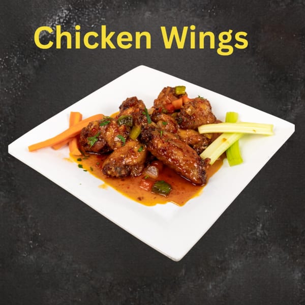 Saucy chicken wings garnished with herbs and peppers, served with carrot and celery sticks on a white plate.