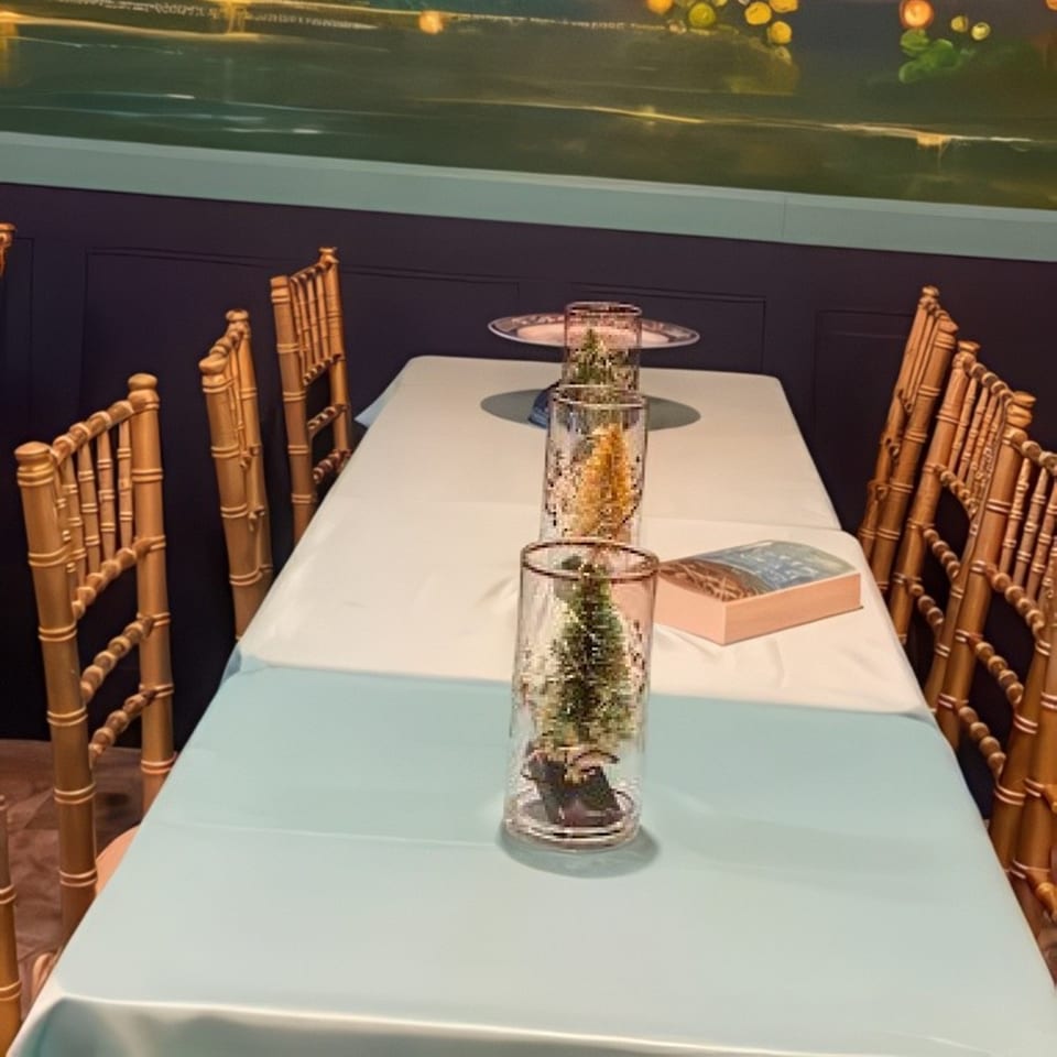 Long dining table set with light blue and white tablecloths, gold chairs, and miniature trees in glass vases.